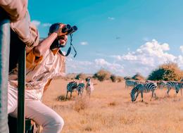 Foto de um homem aparentemente caucasiano, usando binóculos para admirar cada detalhe da natureza em um safári pela África do Sul.