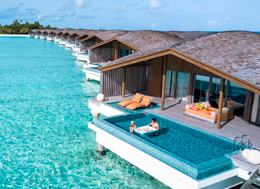 Bangalôs luxuosos sobre águas azul-turquesa cristalinas, alguns com piscinas privativas onde casais relaxam em um cenário idílico de resort tropical.